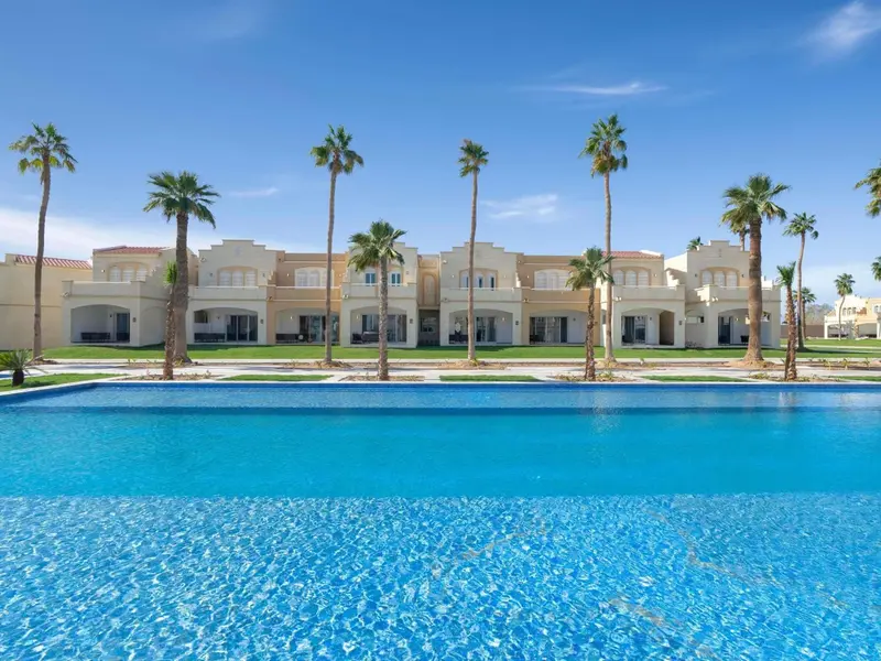 Vue d'une piscine turquoise devant un bâtiment blanc orné de palmiers.