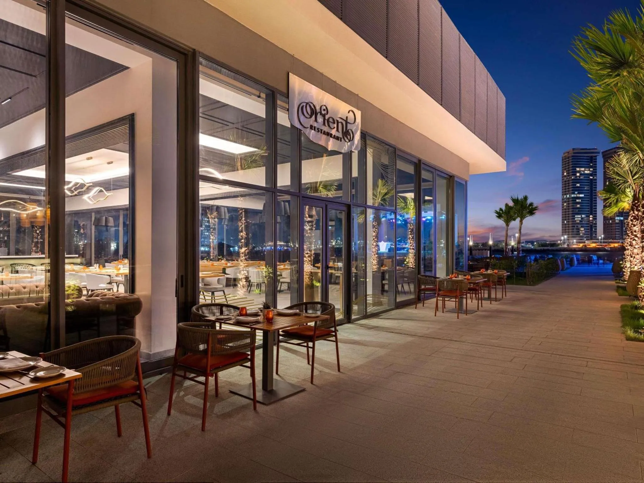 Terrasse de restaurant avec tables et chaises au bord de l'eau au coucher du soleil.