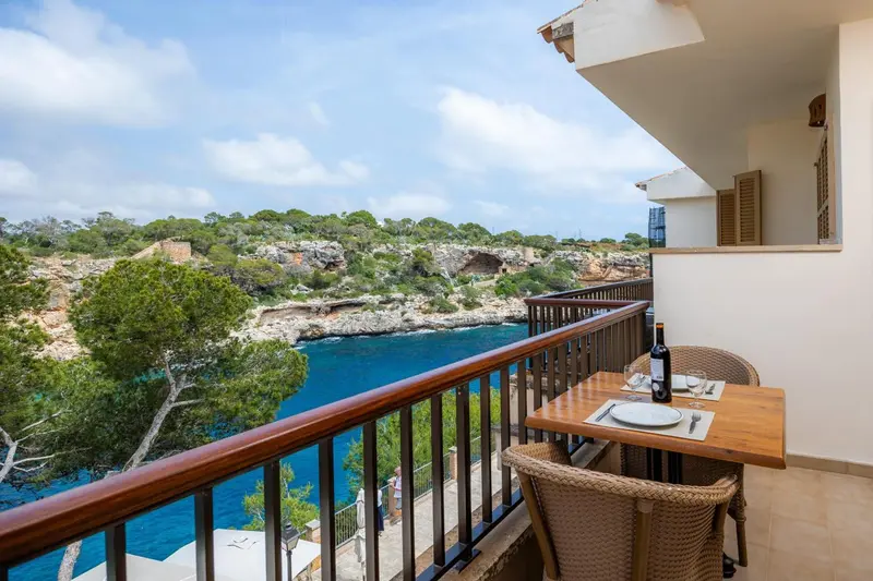 Une terrasse avec une table et des chaises offre une vue sur la mer et la côte rocheuse.