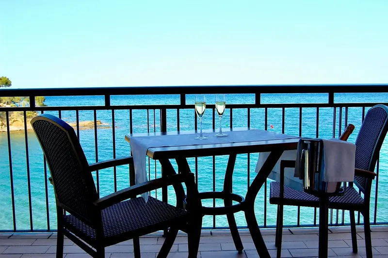 Une table avec deux verres et une bouteille de vin sur un balcon avec vue sur la mer.