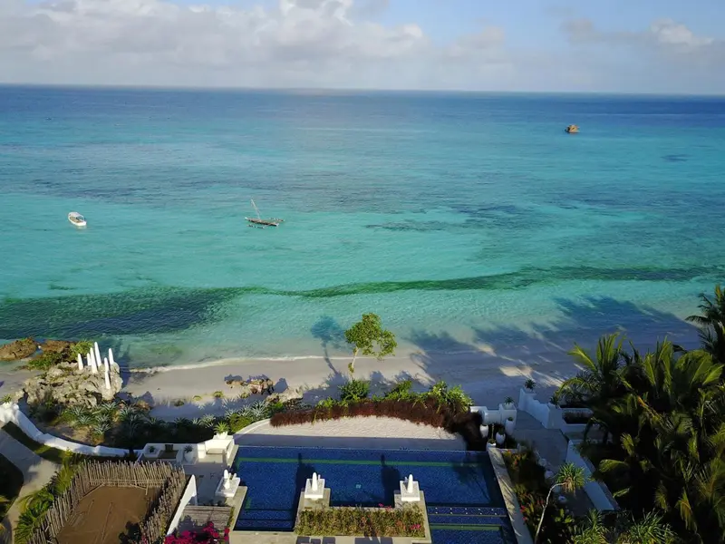 Vue aérienne sur une plage de sable blanc bordée d'une mer turquoise et d'une piscine à débordement.