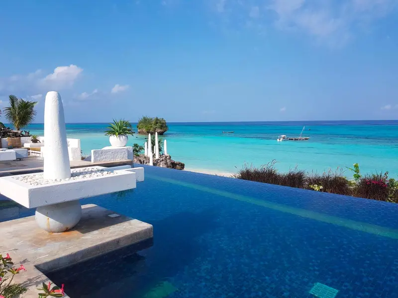 Une piscine à débordement surplombe une mer turquoise et une plage.