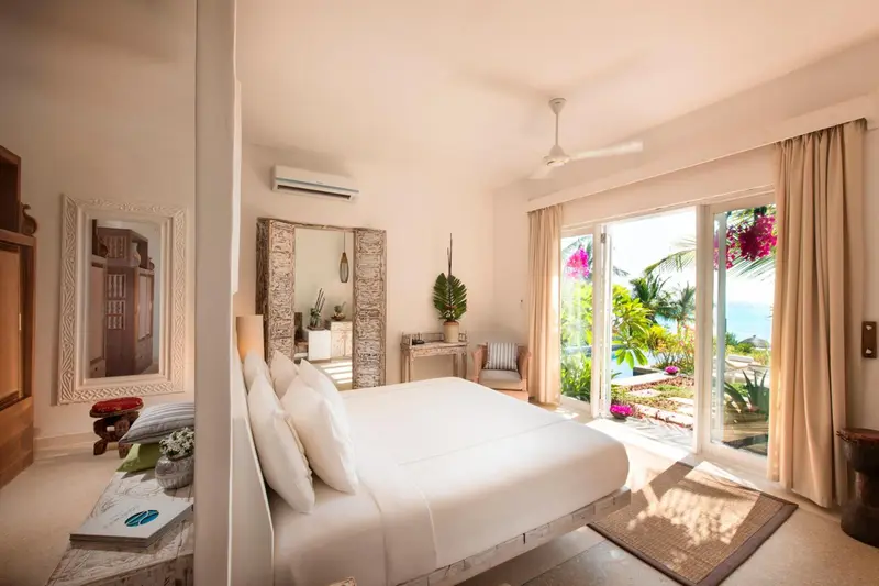 Une chambre lumineuse avec un grand lit blanc et un accès à une terrasse.