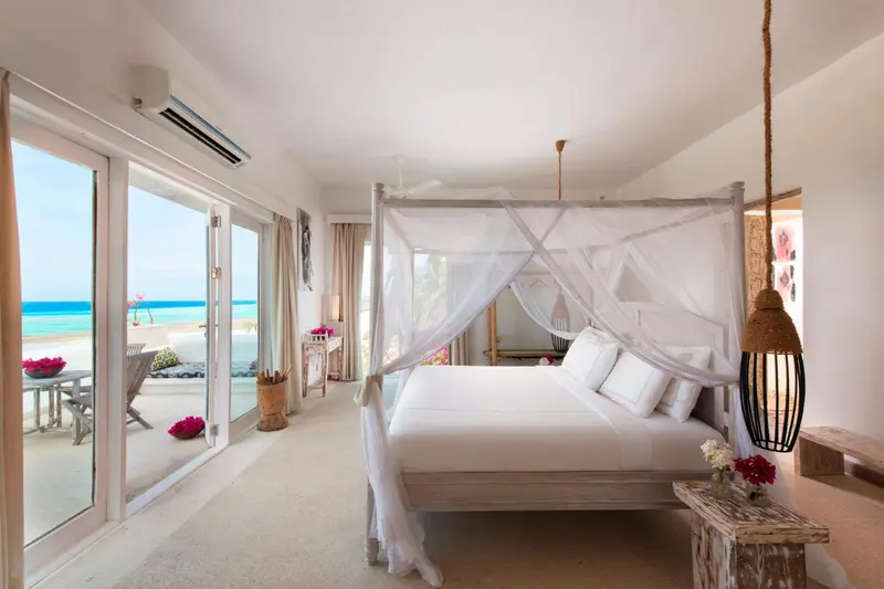 Une chambre lumineuse avec un lit à baldaquin donnant sur une plage.