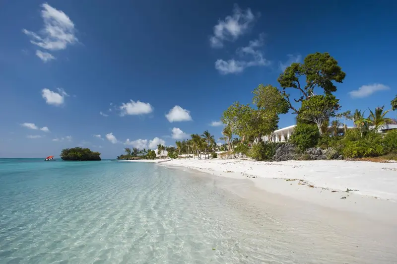 Plage de sable blanc bordée d'une eau turquoise sous un ciel bleu nuageux.