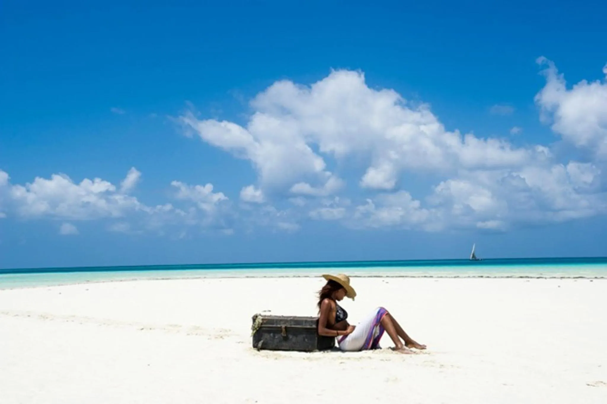 Une femme se repose sur une plage de sable blanc face à la mer turquoise.