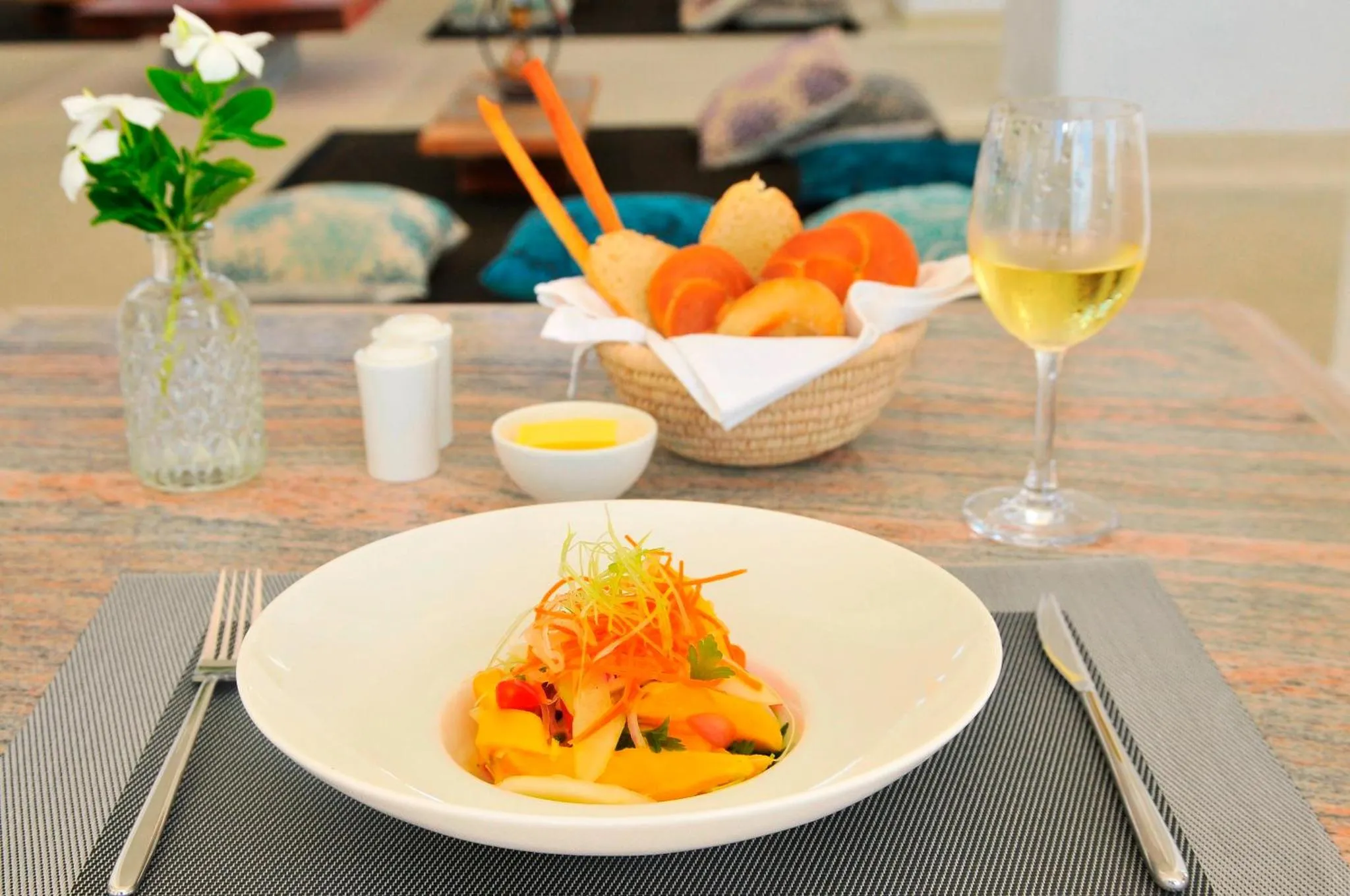 Une assiette de salade colorée est présentée sur une table avec des couverts et une boisson.