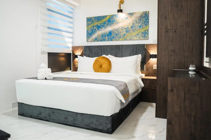 Une chambre lumineuse avec un grand lit recouvert d'une courtepointe blanche et d'un coussin jaune.