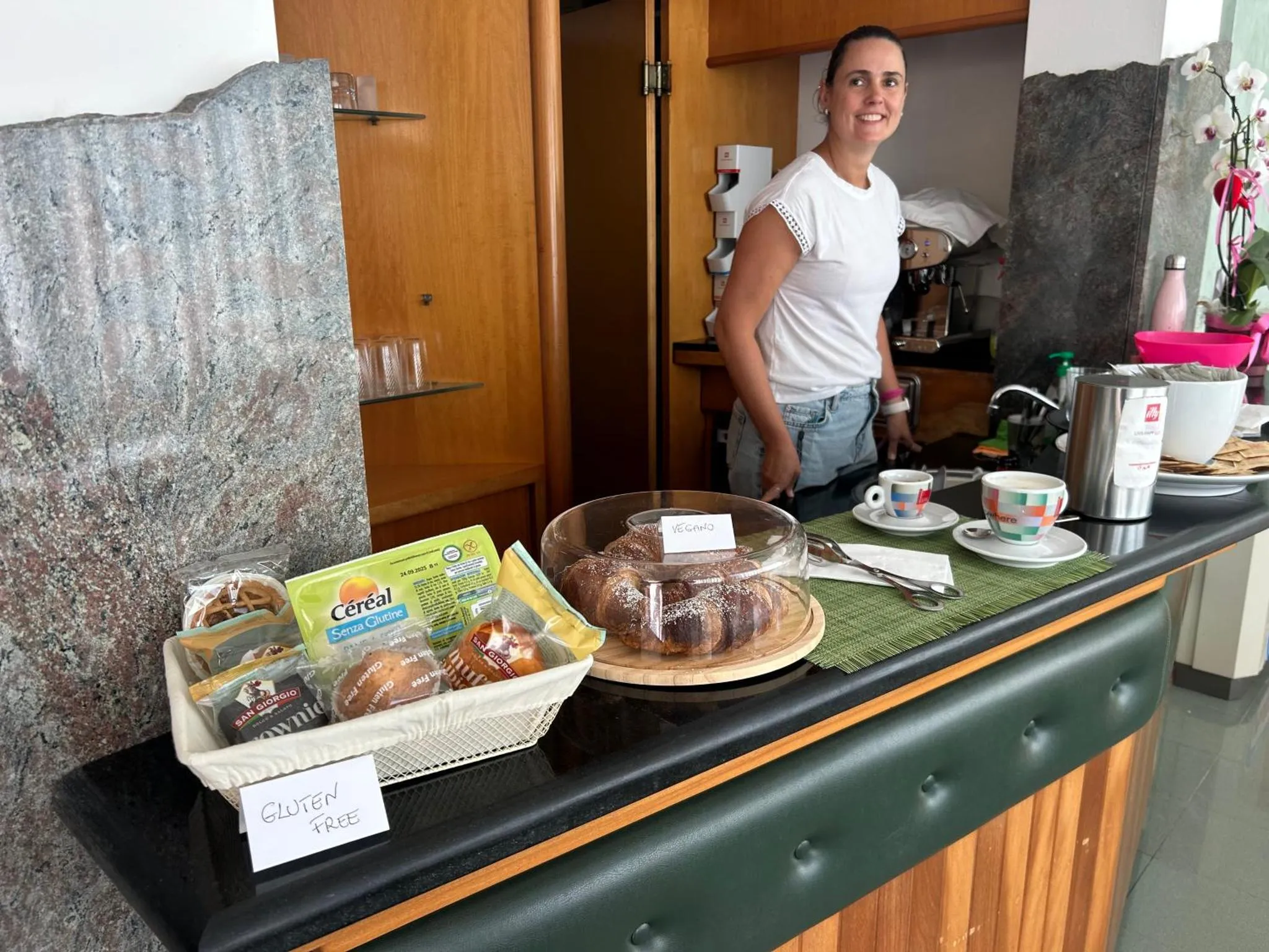 Une personne se tient derrière un comptoir de petit-déjeuner avec des pâtisseries et des boissons.