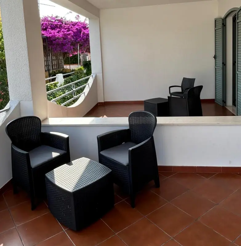 Terrasse avec mobilier en résine tressée et fleurs colorées.