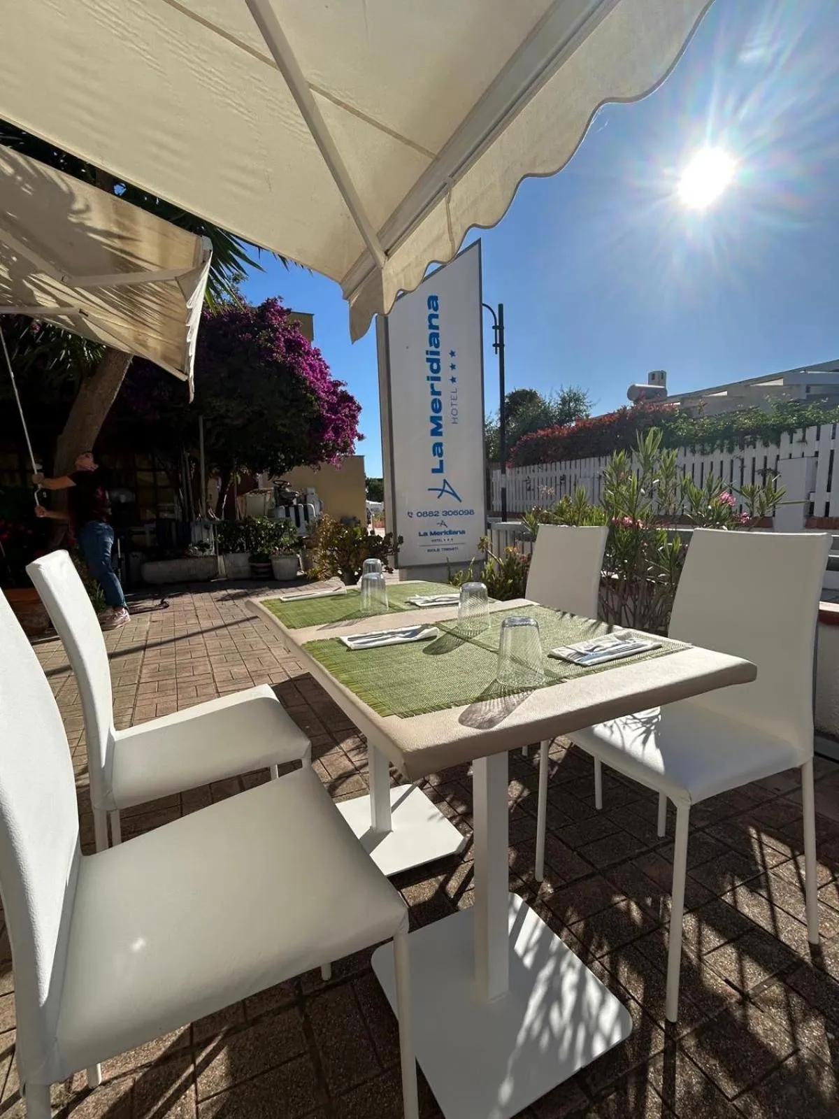 Tables et chaises blanches sur une terrasse ombragée avec des plantes en pots.