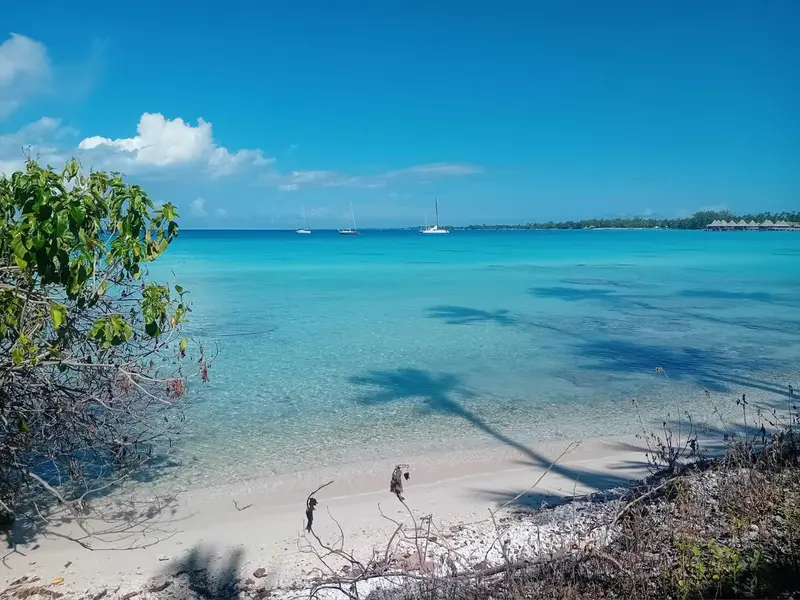 Plage de sable blanc bordée d'une eau turquoise sous un ciel bleu nuageux.