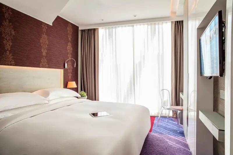 Une chambre d'hôtel lumineuse avec un grand lit et une télévision murale.