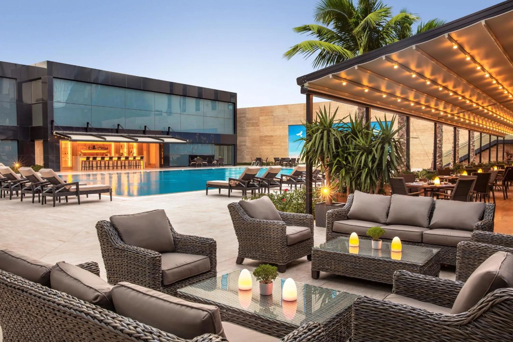 Espace de détente extérieur avec mobilier en rotin et piscine en arrière-plan.