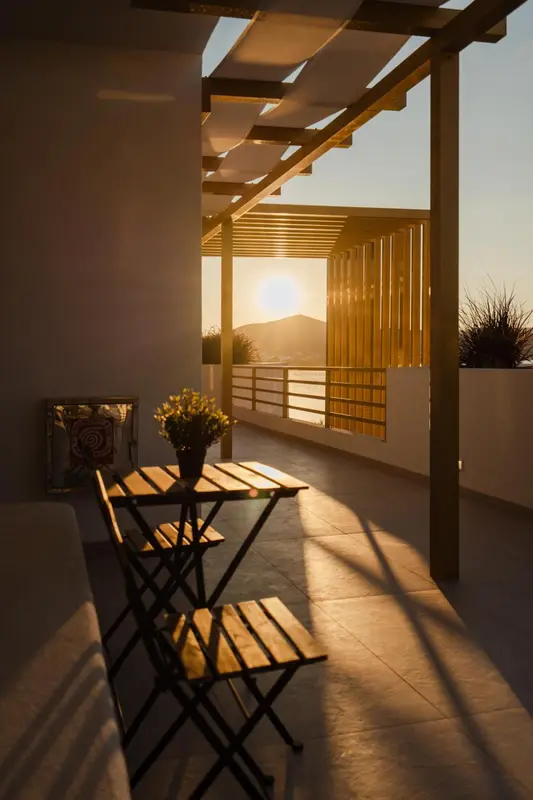 Terrasse ombragée avec table et chaises face à la mer au coucher du soleil.