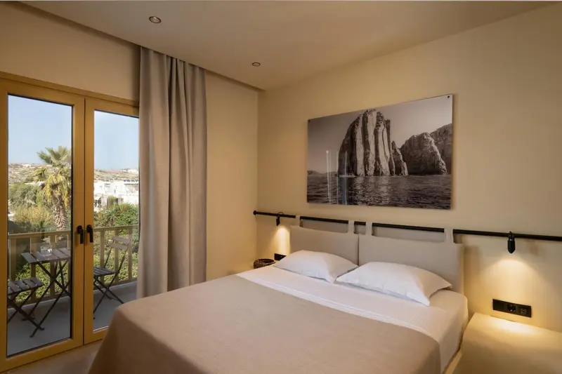 Chambre lumineuse avec un grand lit et une vue sur la mer depuis un balcon.
