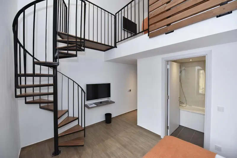 Une chambre avec un escalier en colimaçon menant à une mezzanine.