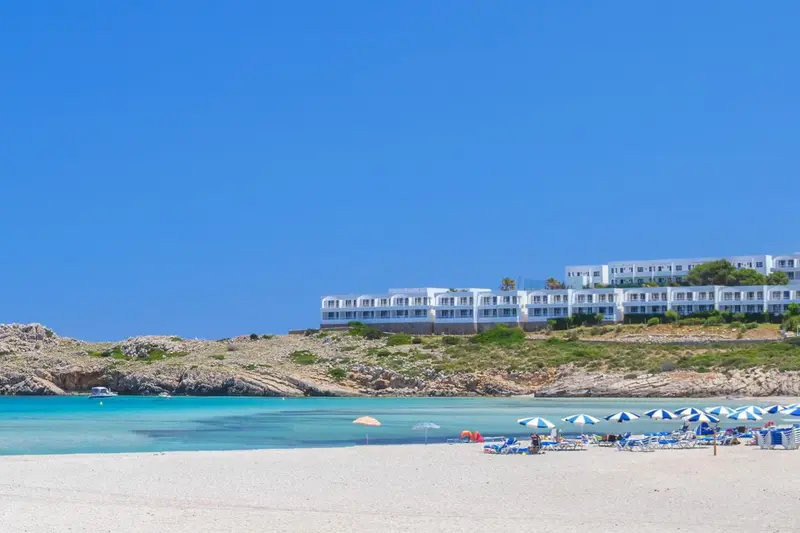 Bâtiment blanc surplombant une plage de sable fin et une eau turquoise.