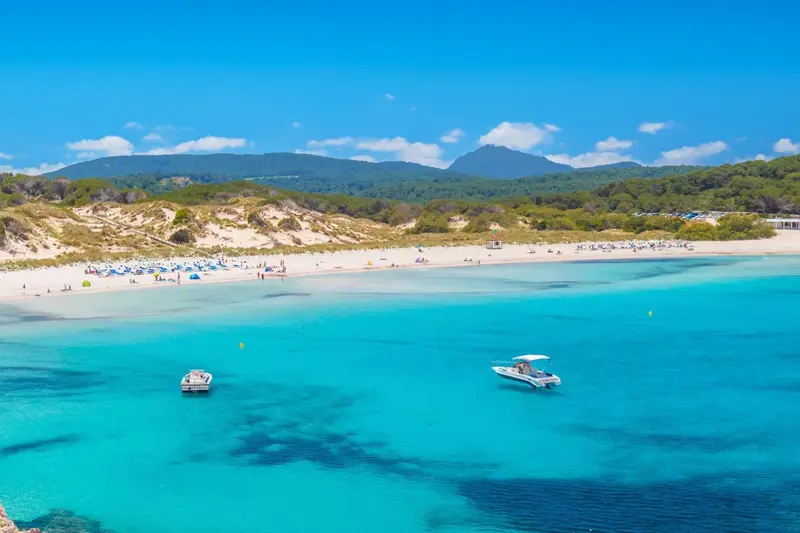 Vue aérienne d'une plage de sable clair bordée d'une eau turquoise et de quelques embarcations.