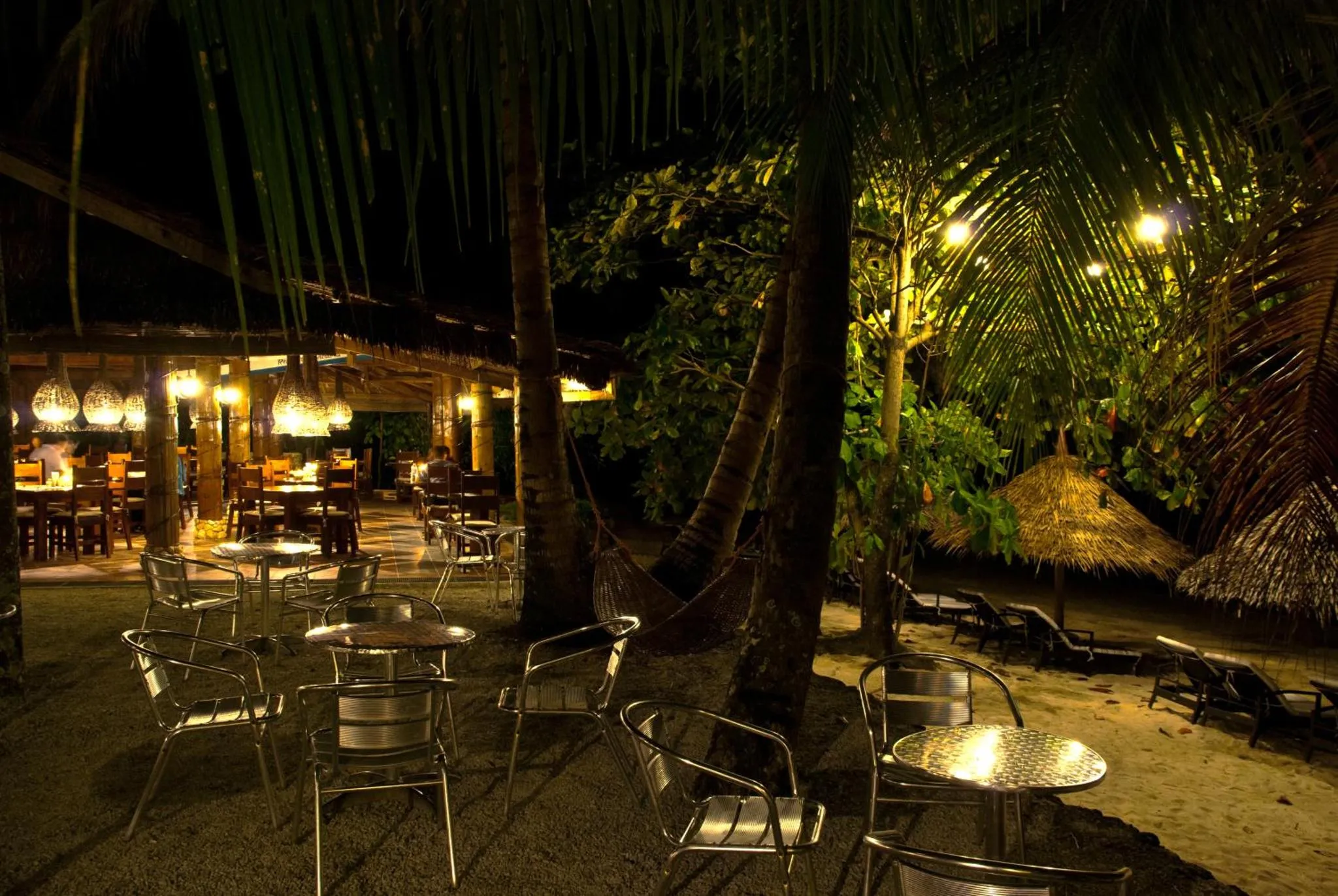 Terrasse lumineuse avec tables et chaises au milieu d'une végétation tropicale.
