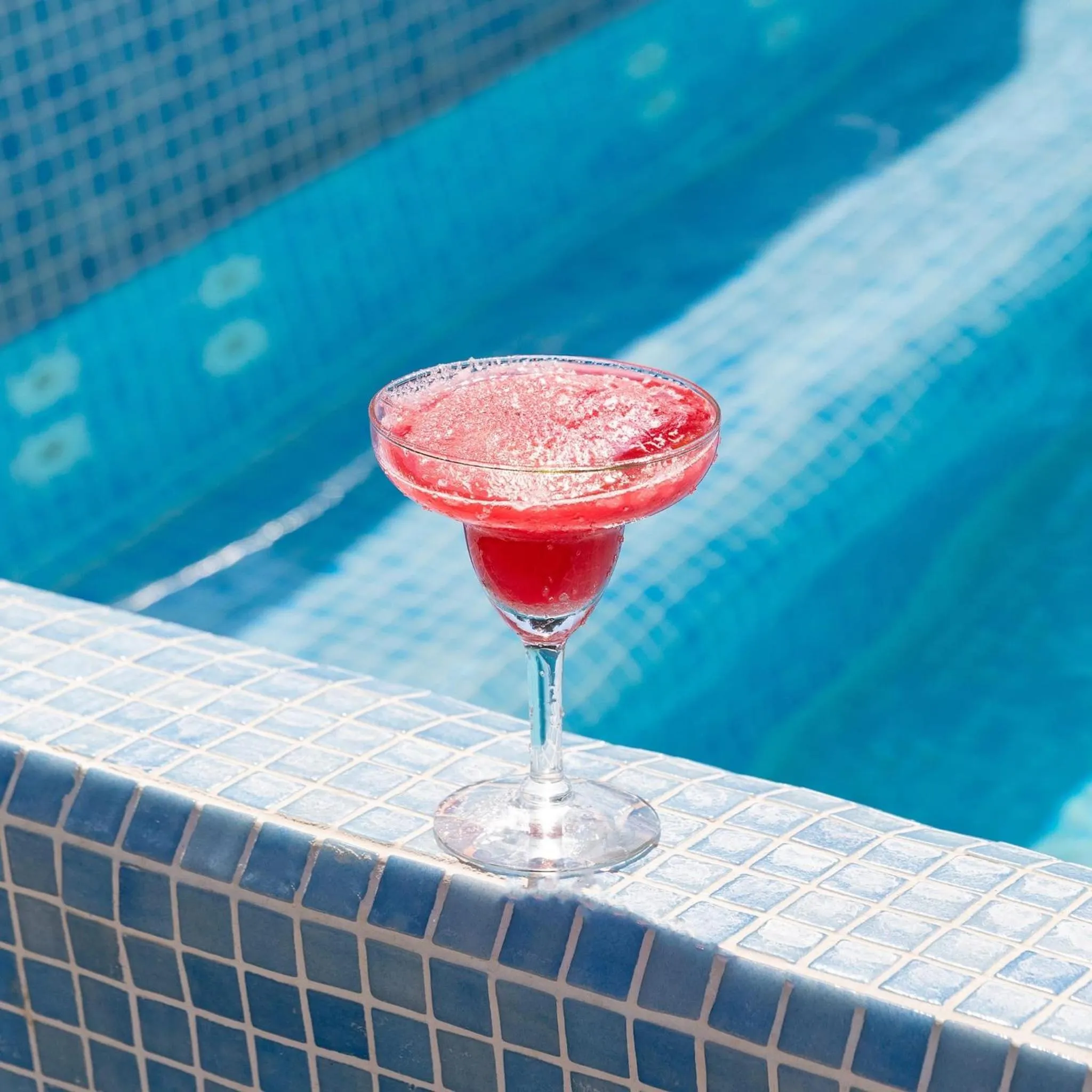 Un cocktail fruité est posé sur le bord d'une piscine carrelée.
