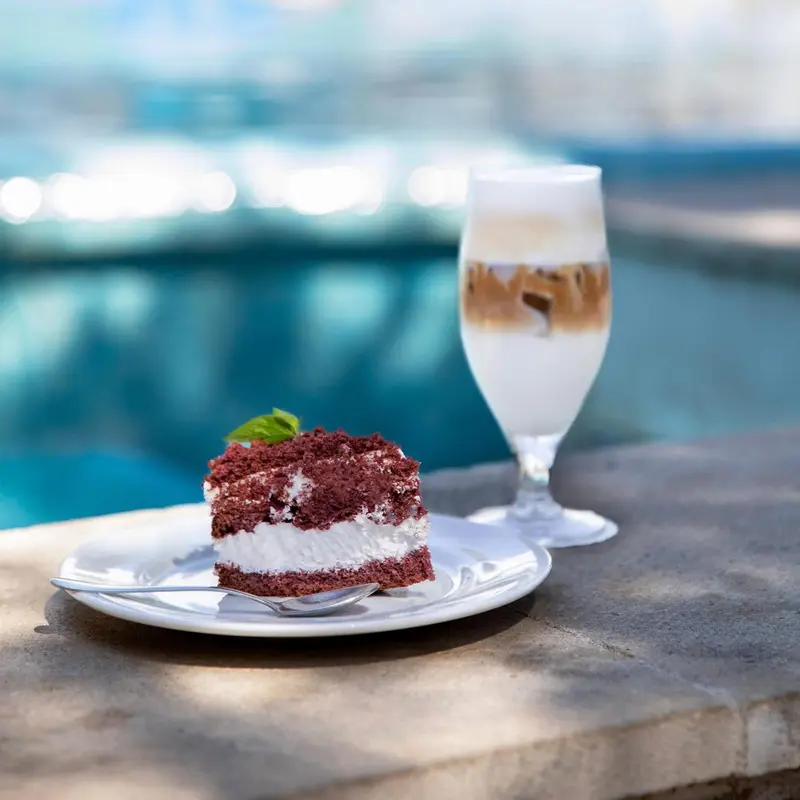 Une pâtisserie rouge et une boisson crémeuse sont présentées sur une table près d'une piscine.