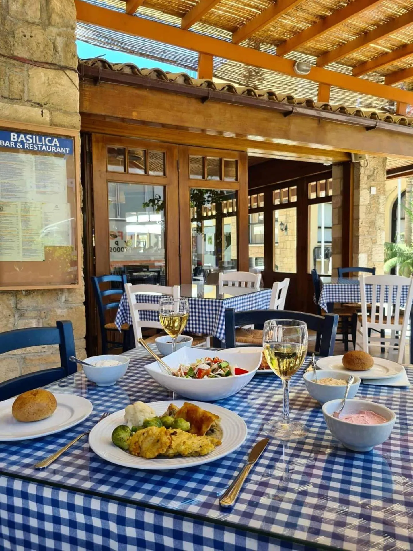 Une table est dressée avec des plats et des boissons sur une terrasse ombragée.