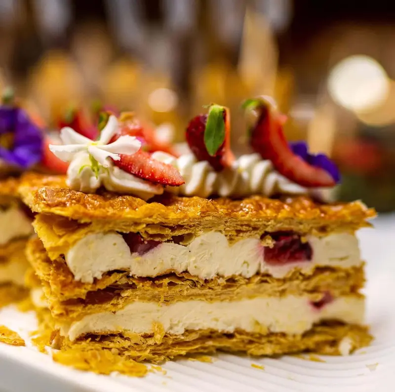 Une part de gâteau à la crème et aux fruits frais est présentée sur une assiette blanche.