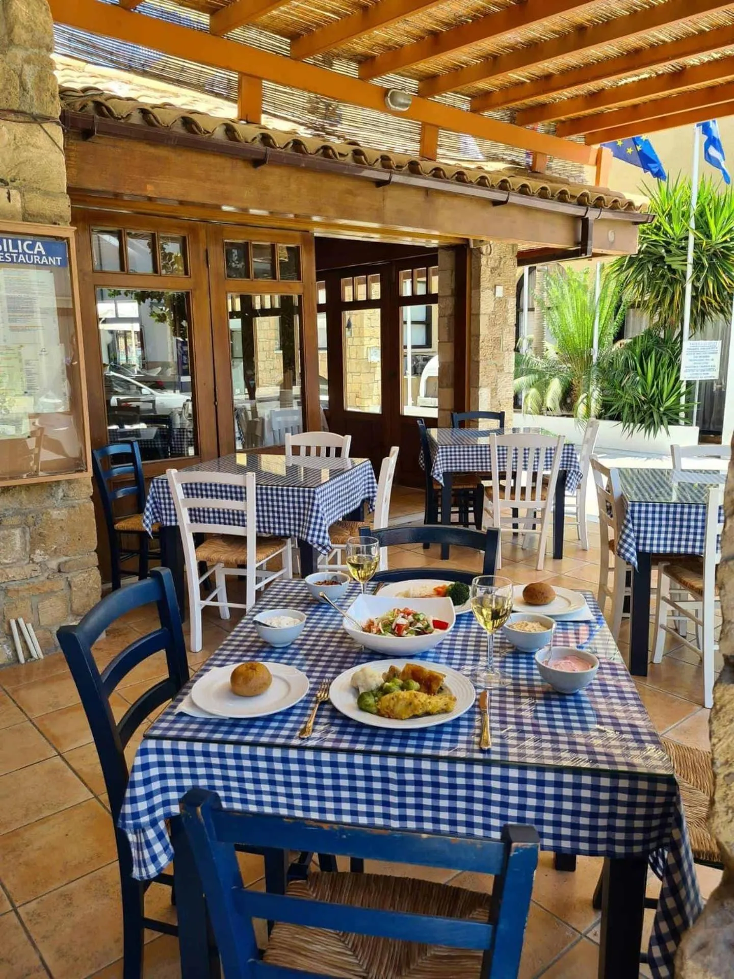 Une table est dressée avec des plats et des boissons sur une terrasse ombragée.
