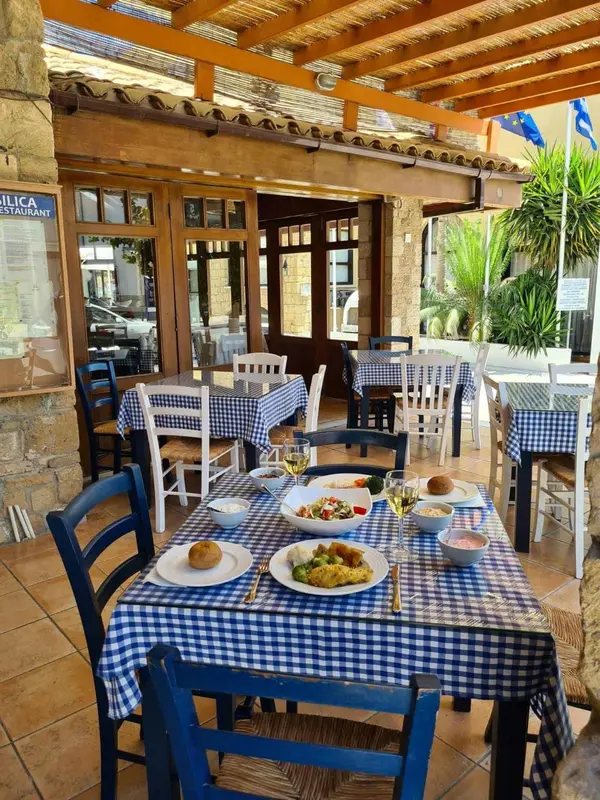Une table est dressée avec des plats et des boissons sur une terrasse ombragée.