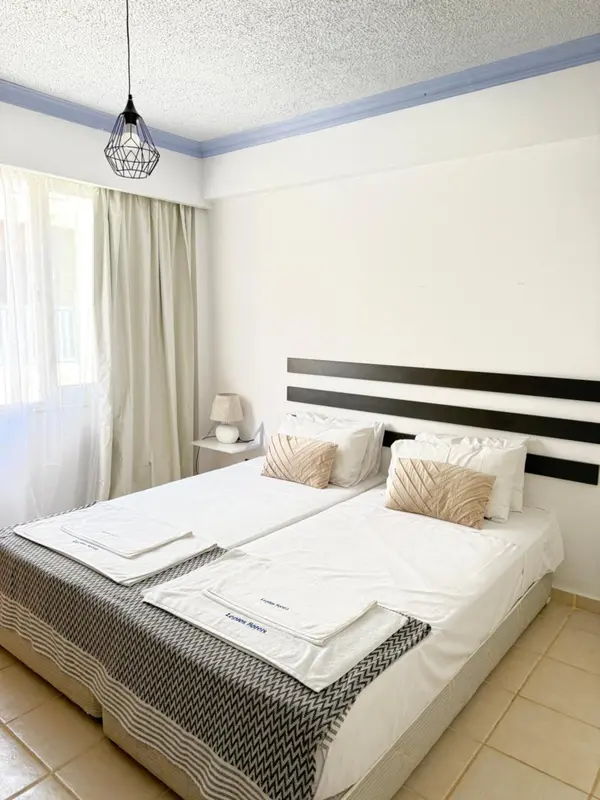 Une chambre lumineuse avec un grand lit recouvert d'une courtepointe blanche et de coussins.