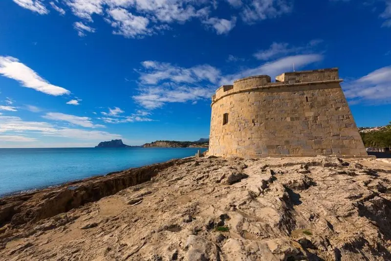 Une tour de pierre ancienne surplombe une côte rocheuse et la mer.