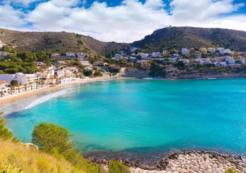 Vue aérienne d'une crique abritée avec une plage de sable et des bâtiments blancs.