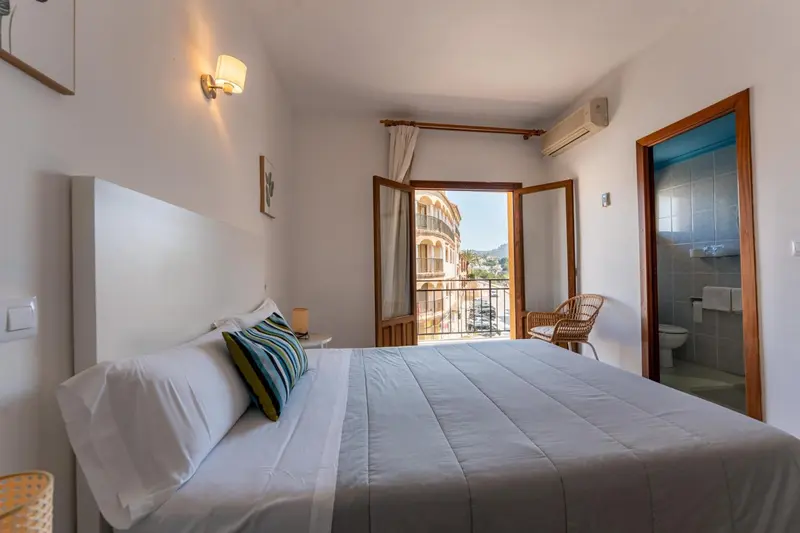 Une chambre lumineuse avec un grand lit et un accès à un balcon.