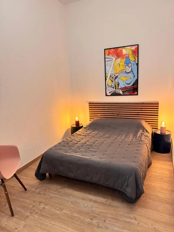 Une chambre sobre avec un lit recouvert d'une couverture grise et une décoration murale colorée.