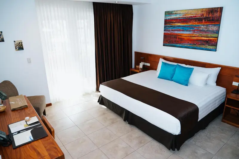 Une chambre lumineuse avec un grand lit recouvert d'une courtepointe blanche et de coussins turquoise.