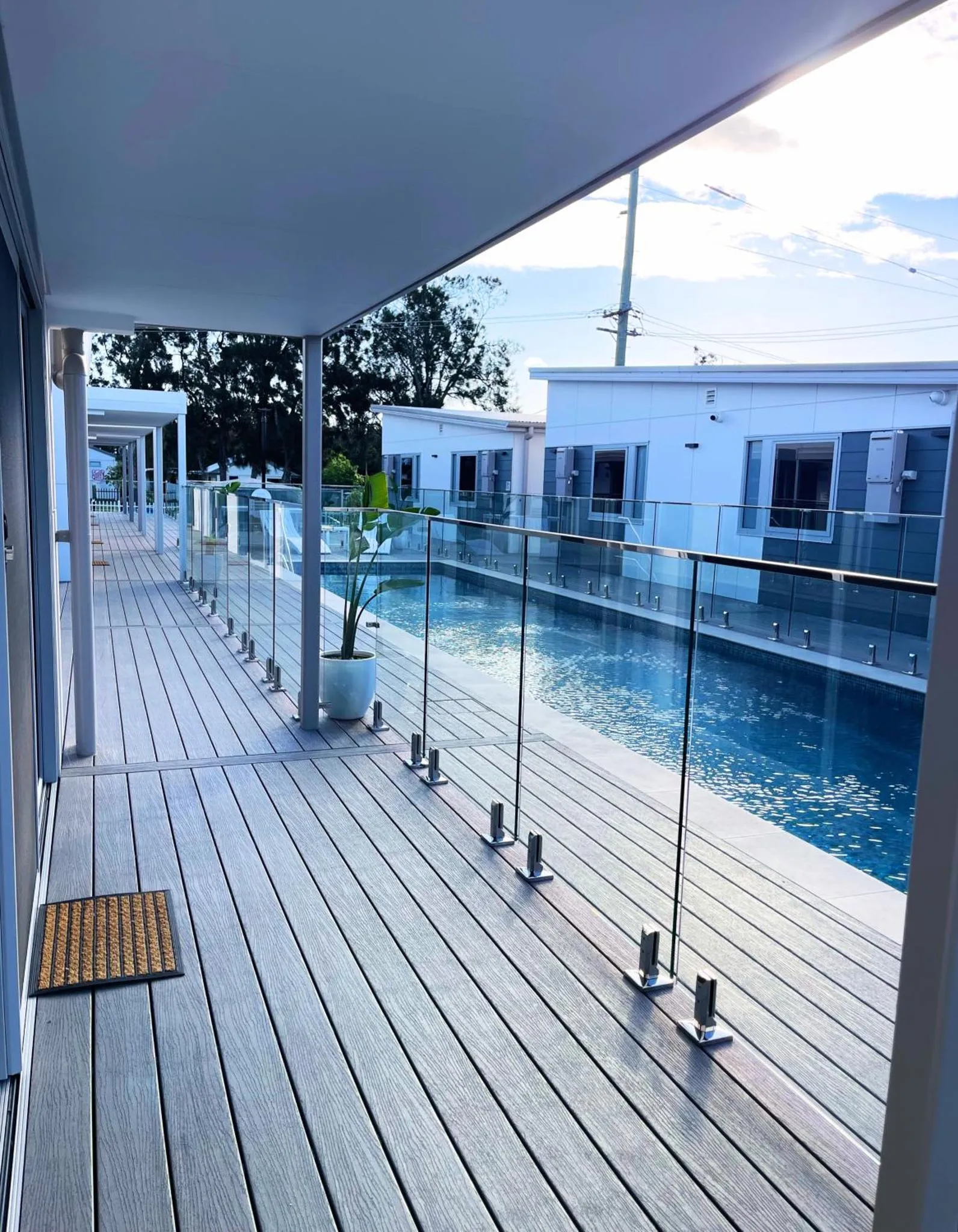 Terrasse en bois avec piscine rectangulaire et garde-corps en verre.