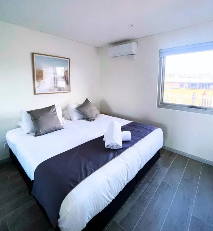 Une chambre avec un grand lit recouvert d'une courtepointe sombre et de coussins gris.