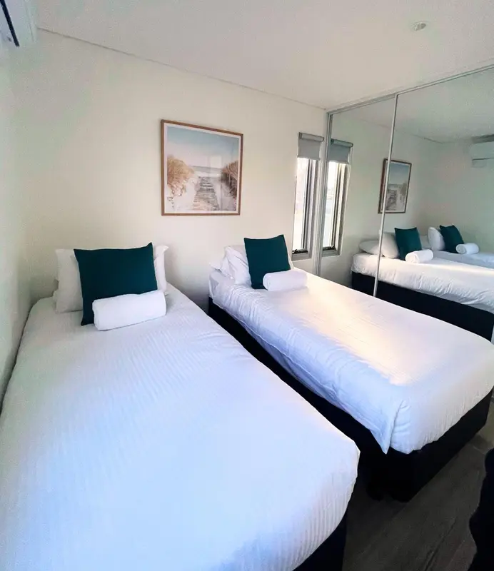 Chambre lumineuse avec deux lits simples et des oreillers verts.