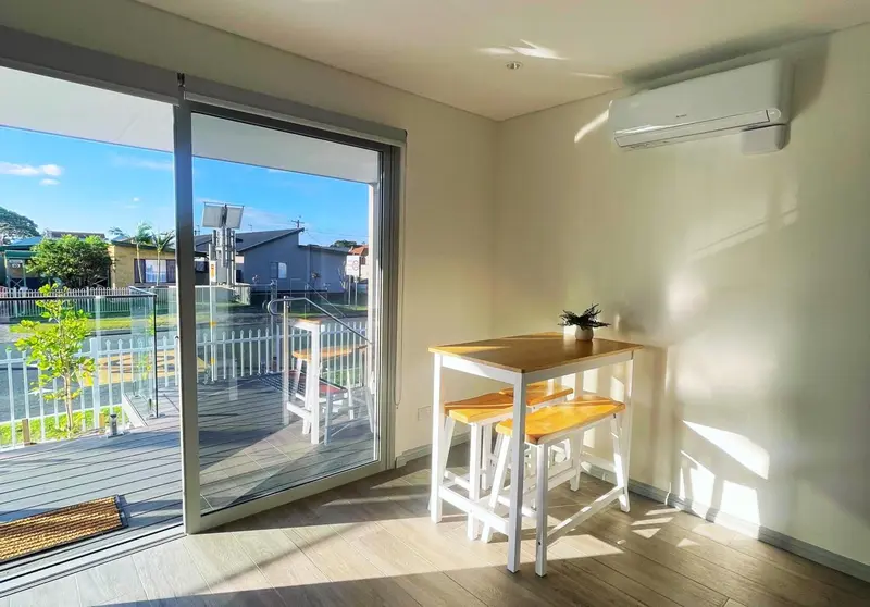 Une table et des tabourets se trouvent devant une baie vitrée donnant sur une terrasse.
