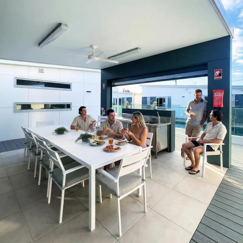 Des convives sont attablés sur une longue terrasse ensoleillée.
