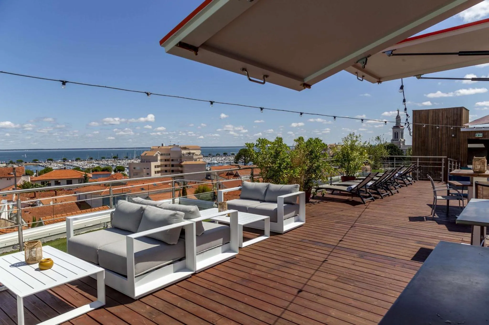 Terrasse aménagée avec des salons et transats offrant une vue sur la mer et la ville.
