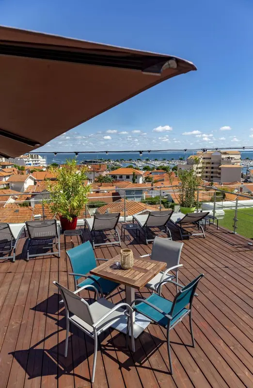 Terrasse aménagée avec tables et chaises offrant une vue sur la ville et la mer.