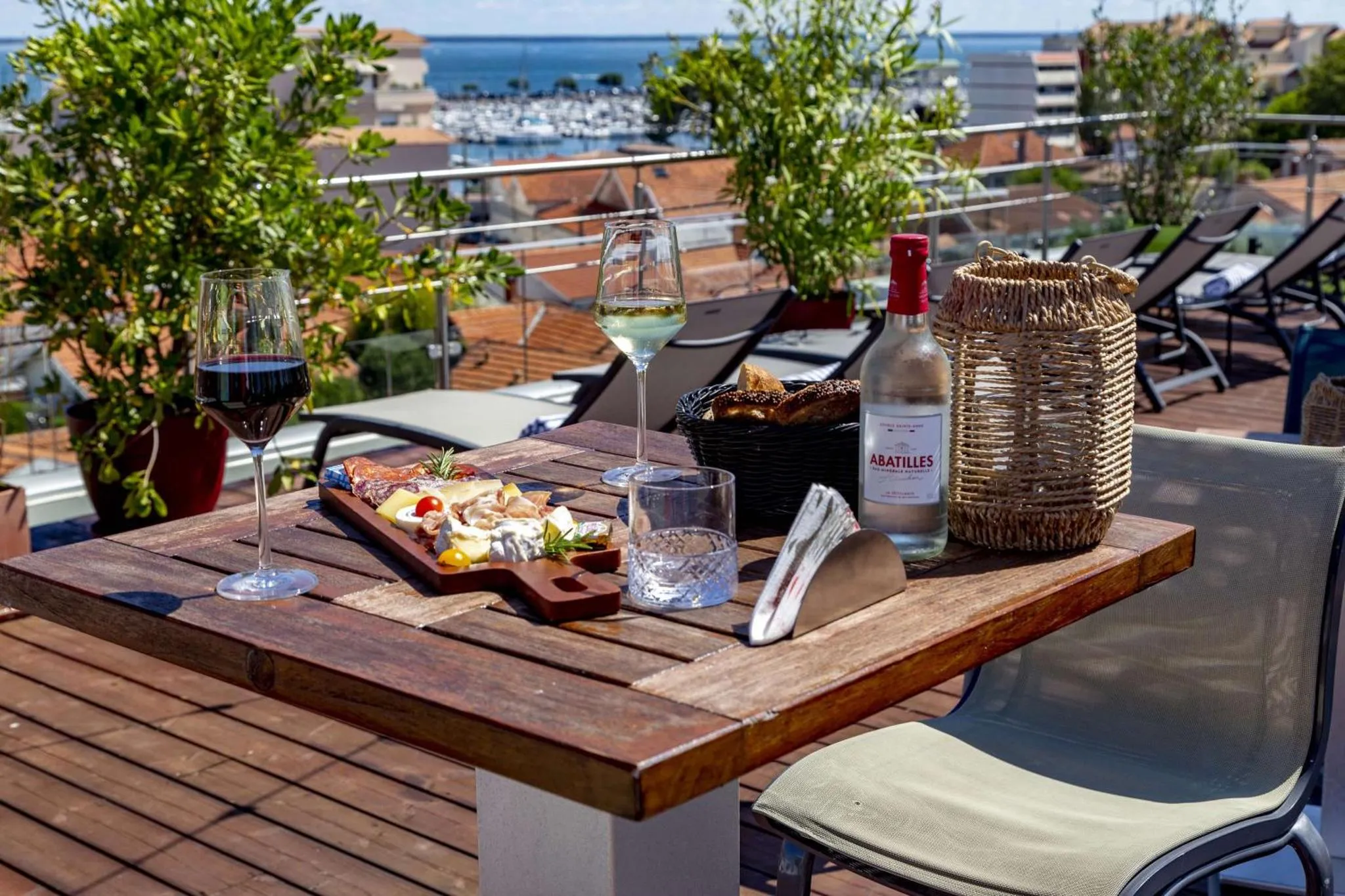 Une table en bois avec des boissons et des amuse-gueules sur une terrasse ensoleillée avec vue sur la mer.