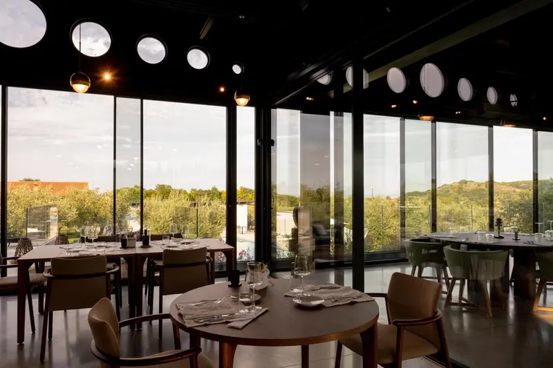Une salle lumineuse avec des tables dressées face à une grande baie vitrée.