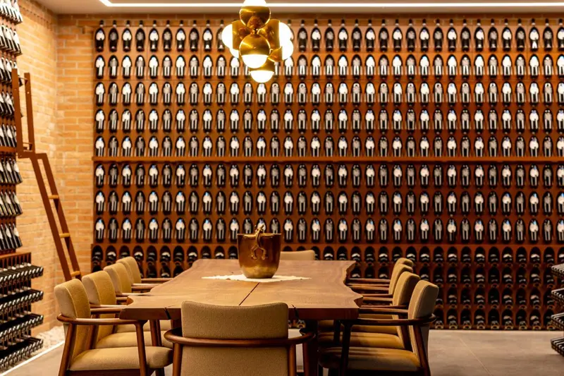 Une table en bois est entourée de chaises dans une cave à vin avec des bouteilles exposées sur les murs.