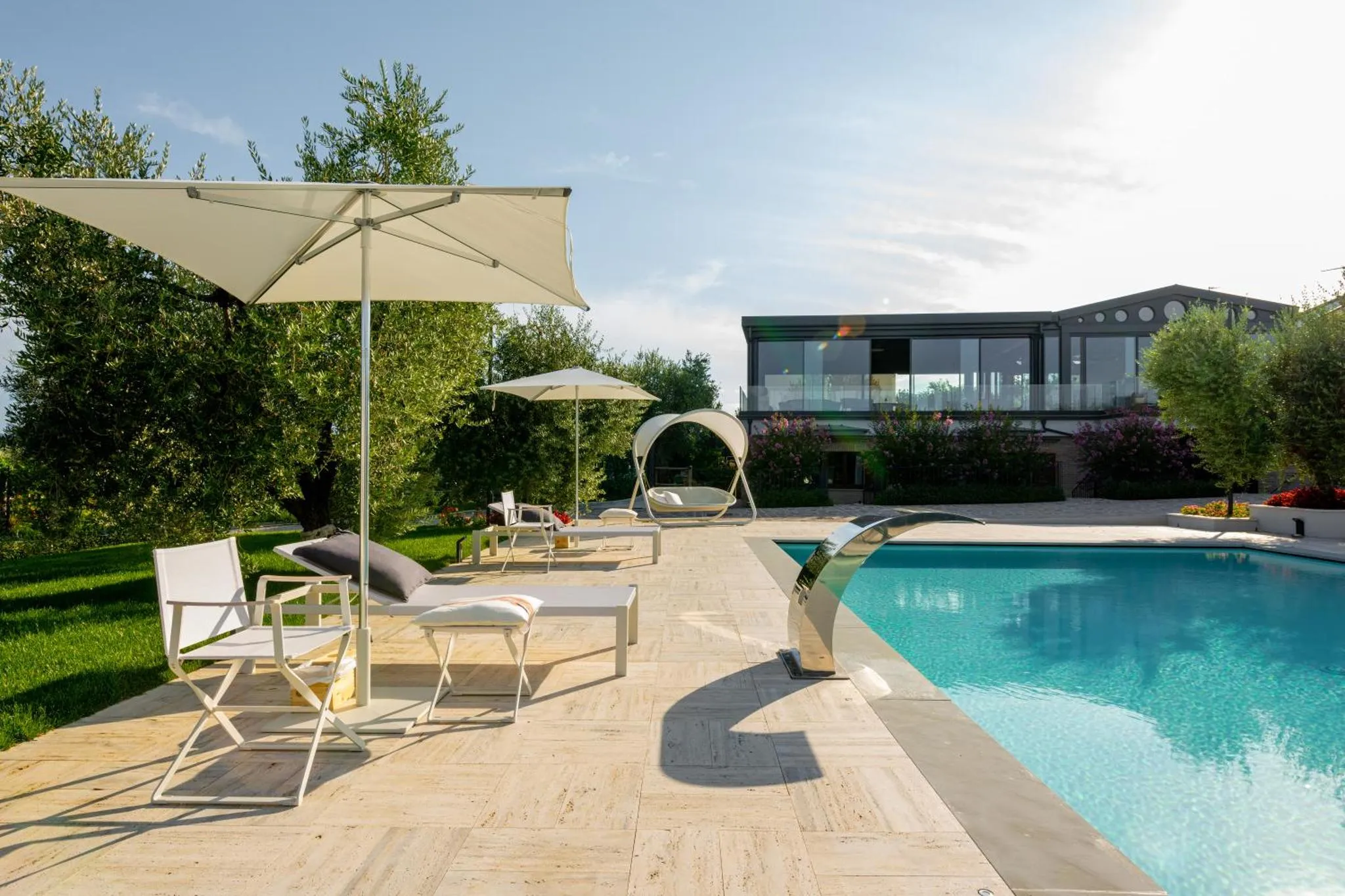 Transats et parasols bordent une piscine rectangulaire au bord d'une pelouse verdoyante.