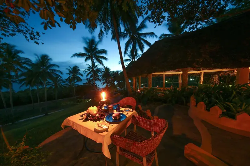 Une table dressée pour un dîner en extérieur, éclairée par des bougies, avec une vue sur la mer au crépuscule.