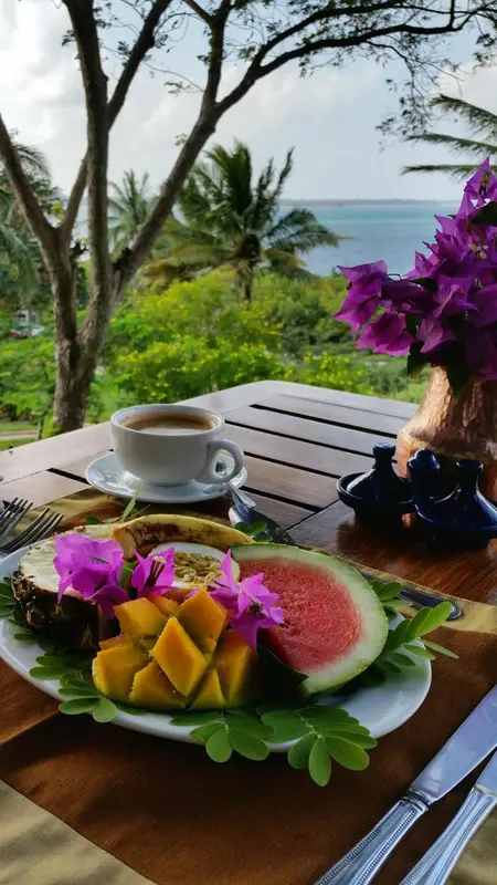 Une table en bois présente une assiette de fruits frais et une tasse de café.