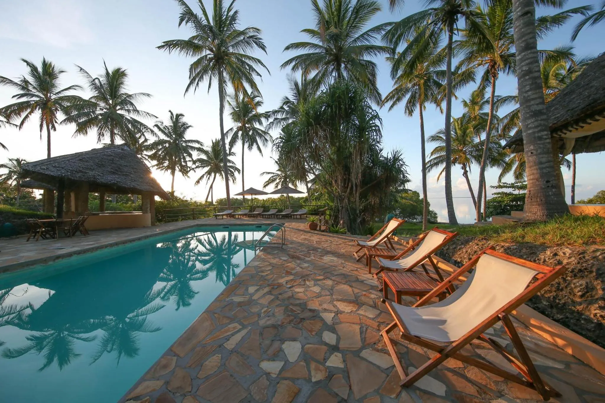 Transats alignés au bord d'une piscine turquoise entourée de végétation tropicale.